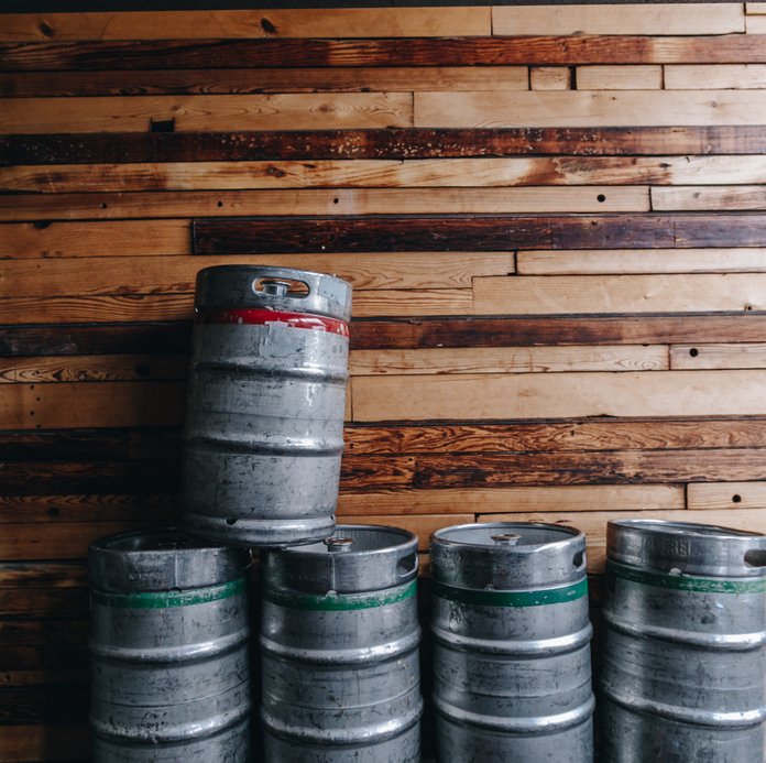 Stacked metal beer kegs against a wooden wall in a rustic setting.